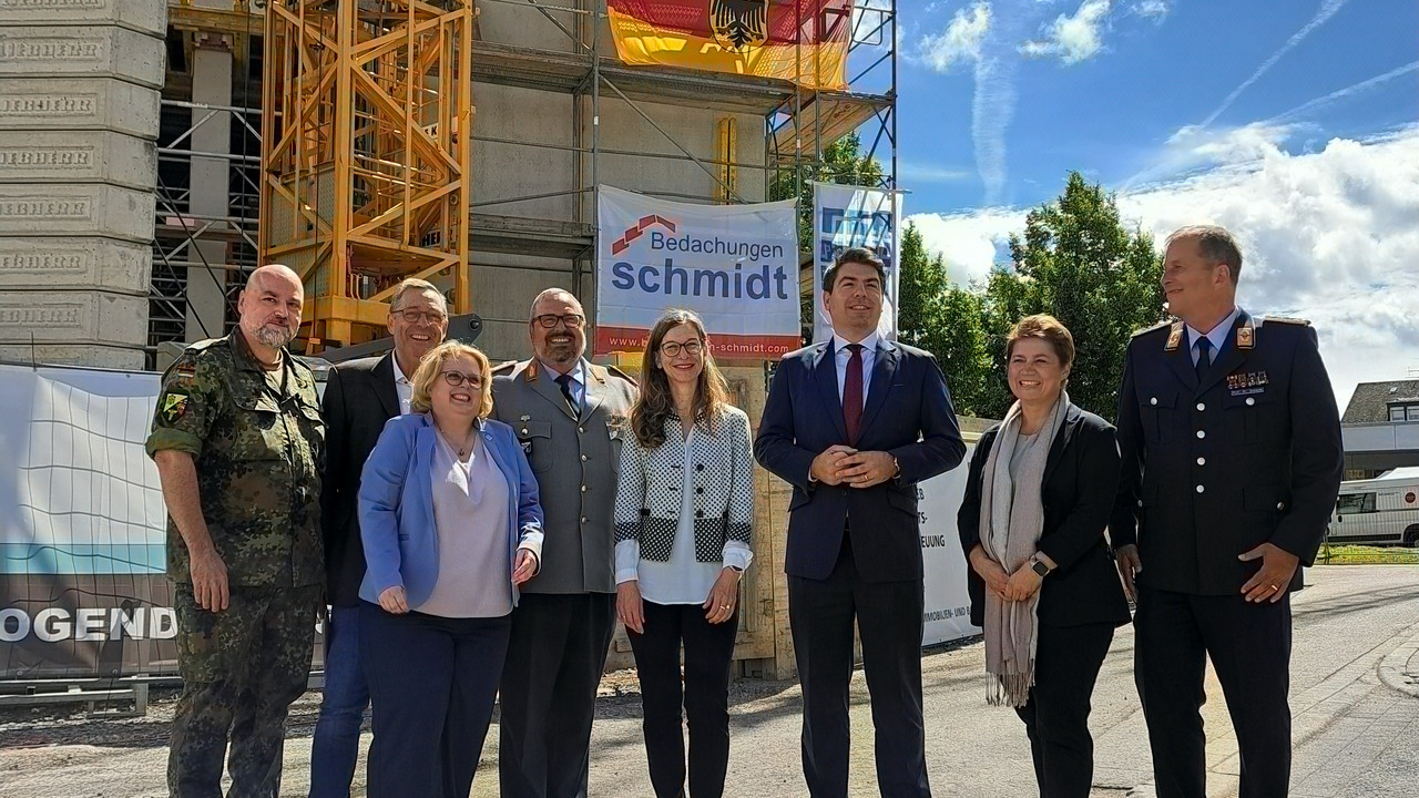 Vor dem Gebäude mit Richtkranz stehen von links: Oberst Knuth Pfeiffer (Bundesamt für Infrastruktur, Umweltschutz und Dienstleistungen der Bundeswehr – BAIUDBw -),Manfred Hill, Leiter der LBB-Niederlassung Koblenz, Elena Kraus (Stv. Geschäftsführerin Landesbetrieb LBB), Generalarzt Dr. med. Jens Diehm (Kommandeur und Ärztlicher Direktor Bundeswehr-Zentralkrankenhaus Koblenz), Janine Färber (Abteilungsleiterin im Amt für Bundesbau Rheinland-Pfalz), Thomas Hitschler (Parlamentarischer Staatssekretär beim Bundesminister der Verteidigung), Nancy Sprock-Mahlo (Leiterin des Kompetenzzentrums Baumanagement Wiesbaden des BAIUDBw) und Oberstarzt Prof. Dr. med. habil. Robert Schwab.
