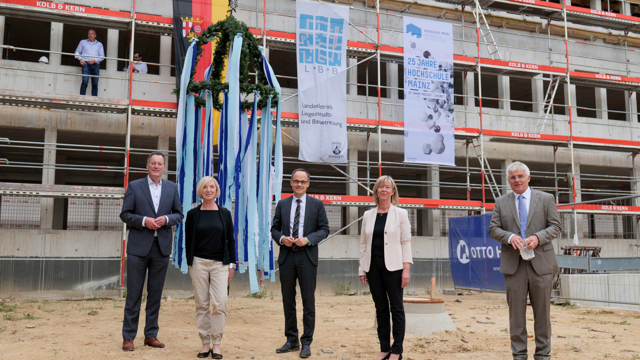 Auf dem Bild sieht man Michael Ebling, Oberbürgermeister der Landeshauptstadt Mainz, Hochschulpräsidentin Prof. Dr. Susanne Weissman, Wissenschaftsstaatssekretär Dr. Denis Alt, Finanz- und Bauministerin Doris Ahnen und Holger Basten, Geschäftsführer des Landesbetriebs LBB. Sie stehen vor dem Rohbau für den 2. Bauabschnitt. Auf dem Gerüst im Hintergrund steht Albert Köberlein, Bauleiter der Fa. Otto Heil, der den Richtspruch ausbrachte.